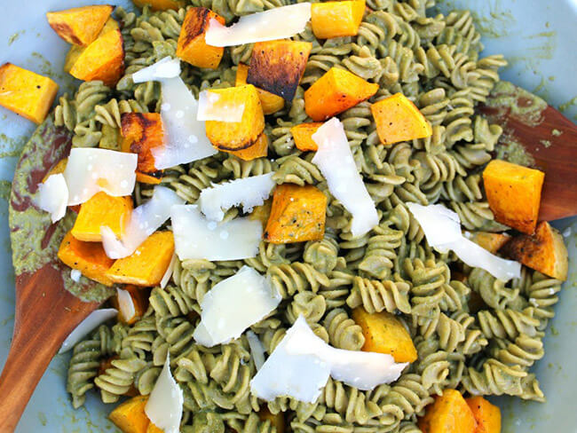 Pesto pasta with roasted butternut squash topped with cheese with a wooden spoon