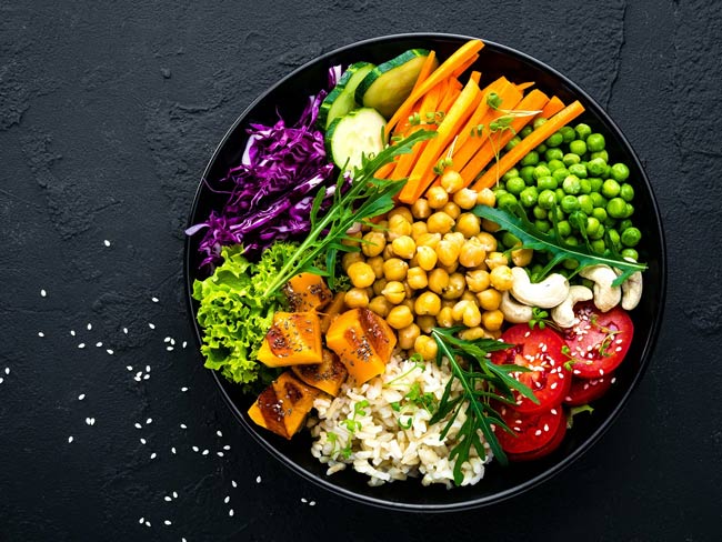 Bowl with brown rice, cucumber, tomato, green peas, red cabbage, chickpea, fresh lettuce salad and cashew nuts.