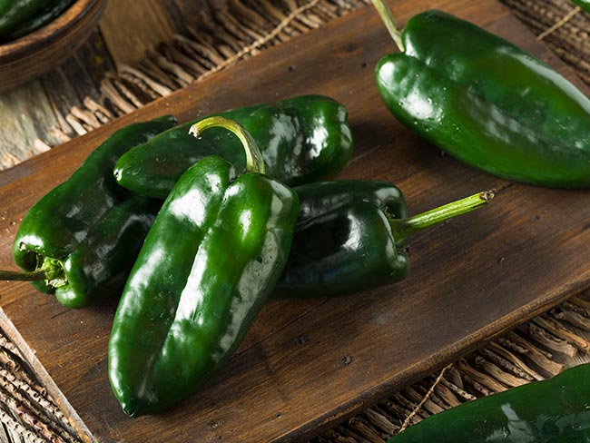 Green poblano chilis on a wooden cutting board.