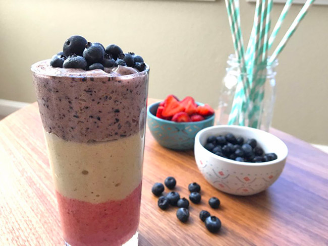 Red, white, and blue layered banana ice cream in a clear glass on a table.