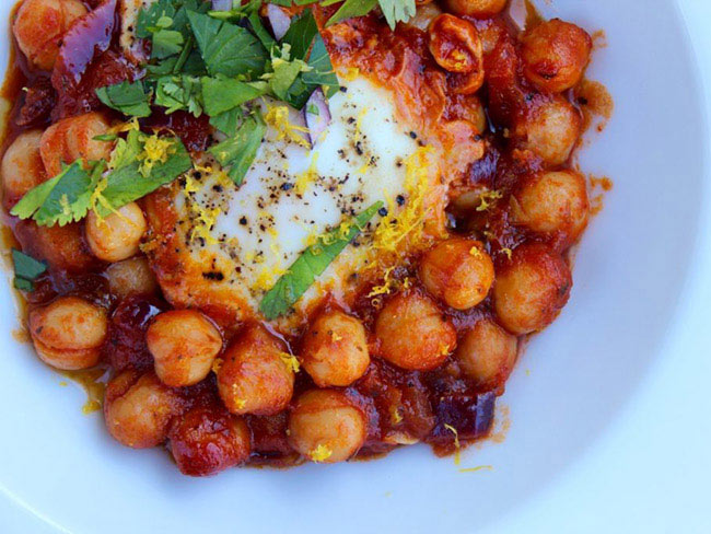 Shakshuka with chickpeas and lemon topped with an egg and garnished with fresh cilantro.