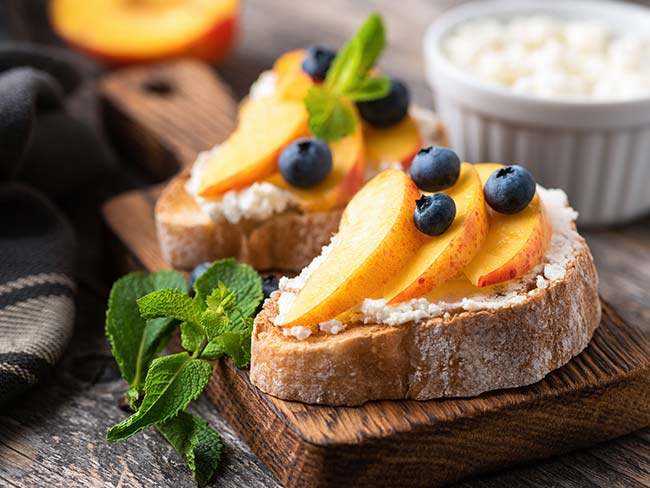 Sliced nectarines on a slice of crostini with goat cheese spread on it.