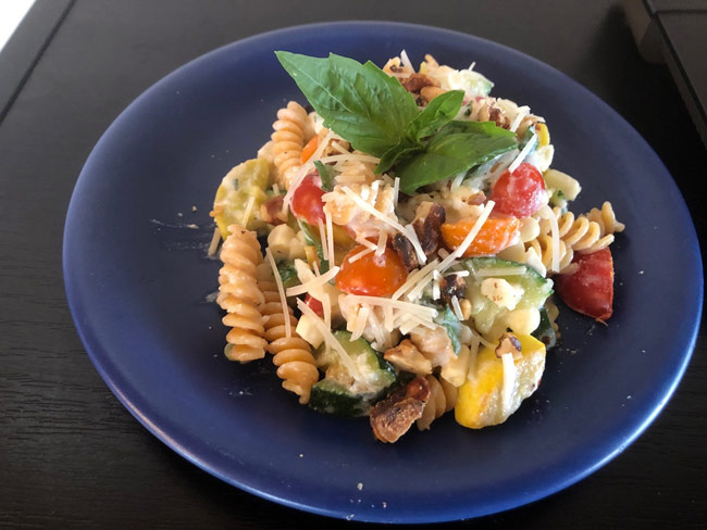 Pasta and colorful vegetables with grated Parmesan cheese on blue plate