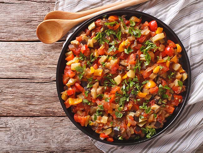 A bowl of ratatouille with onions, red and orange peppers, topped with fresh cilantro.