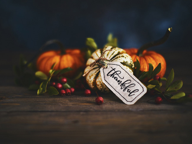 Festive Thanksgiving arrangement, with a few small pumpkins on a wooden table and "thankful" label attached to pumpkin