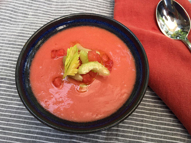 Watermelon and tomato gazpacho served in a black bowl with a spoon garnished with basil