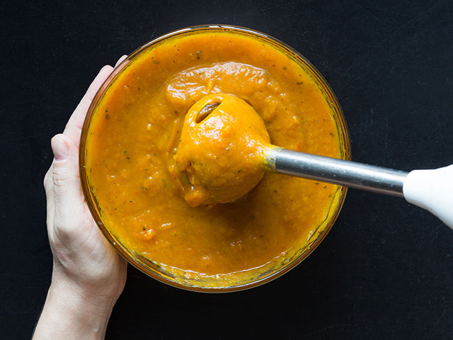 Woman's hands pureeing soup with a hand-held blender 